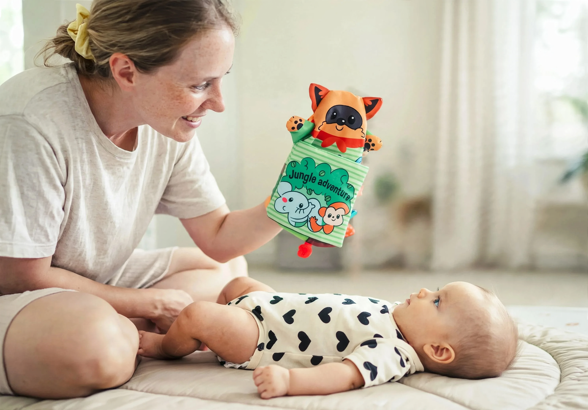Baby watching a raccoon hand puppet on a jungle cloth book with a parent