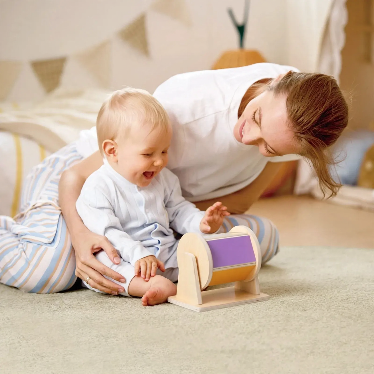 Baby reaching for a wooden sensory drum with a parent nearby